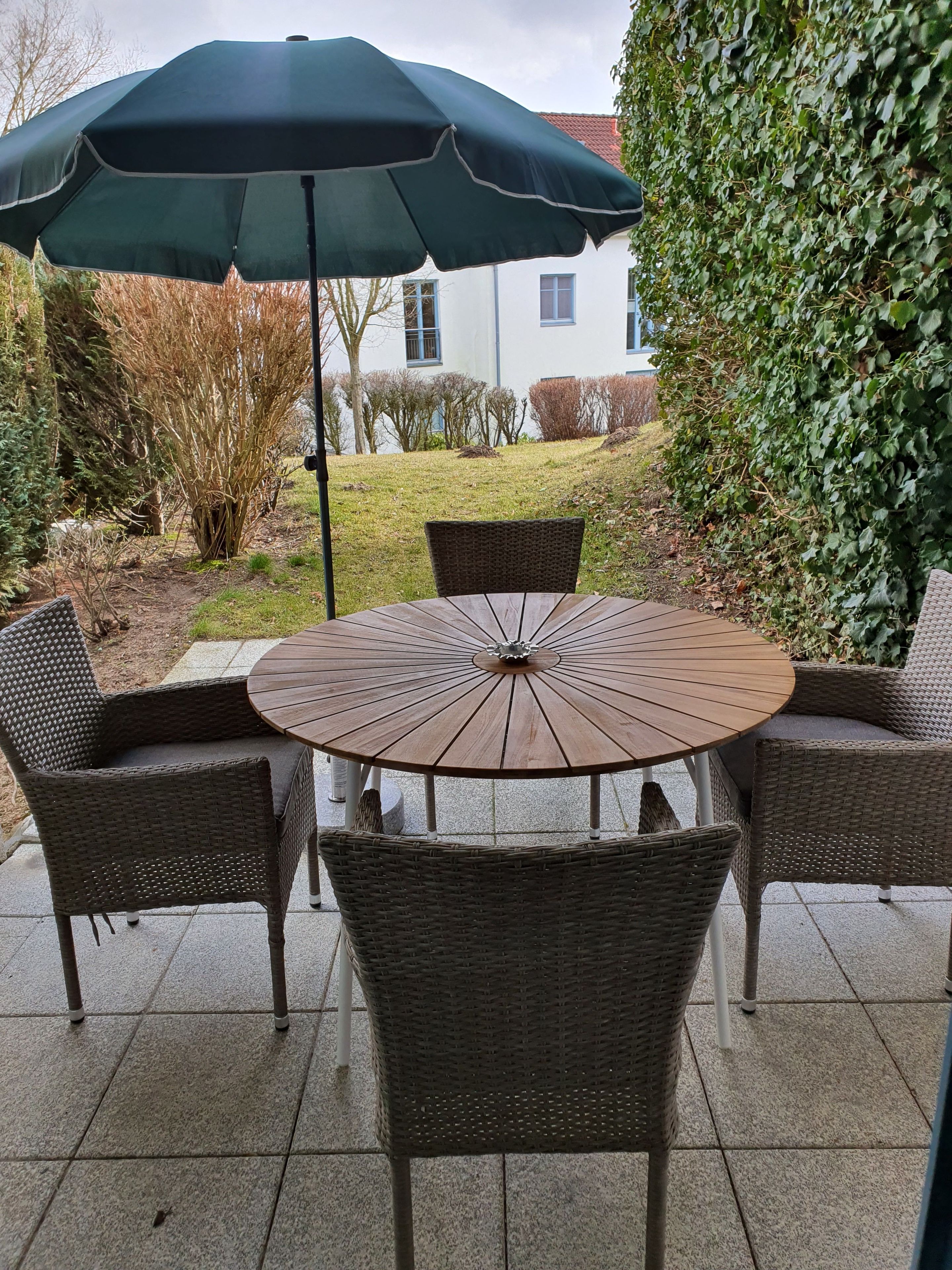 Une table ronde entourée de chaises en osier et surmontée d’un parasol vert.