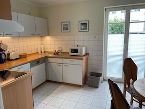 Une cuisine avec des meubles blancs, un four à micro-ondes, un grille-pain et un évier. Deux tableaux encadrés sont accrochés au mur.