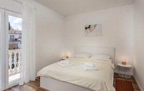 Un dormitorio con cama, dos lámparas de noche, un cuadro en la pared y un balcón con barandilla.