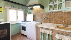 Une cuisine équipée d’une cuisinière, d’un four et d’un évier. Il y a une fenêtre avec des rideaux et un pare-feu en carrelage.