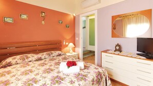 Une chambre à coucher avec une couvre-lit à motifs floraux, une tête de lit en bois, une lampe de chevet, une commode avec un miroir et un téléviseur.