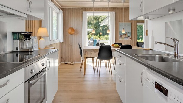Een moderne keuken met een eethoek, met roestvrijstalen apparatuur, houten vloeren en uitzicht op groen.