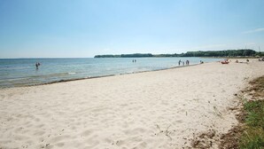 Een breed zandstrand met rustig water, een heldere lucht en een veraf gelegen bebost gebied.