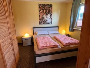 Une chambre à coucher avec un lit, deux tables de chevet, une commode, une affiche au mur et une fenêtre avec des rideaux.
