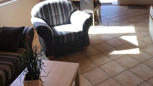 A living room with a sofa, armchair, and a small table with a plant. There is a dining area with chairs and a table, and a balcony with a railing. - Apartment 1 - Apartment 1 (72389) (Lychen)