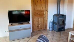A room with a television on a wooden cabinet, a wooden door, and a wood-burning stove. - Apartment 1 - Apartment 1 (72389) (Lychen)