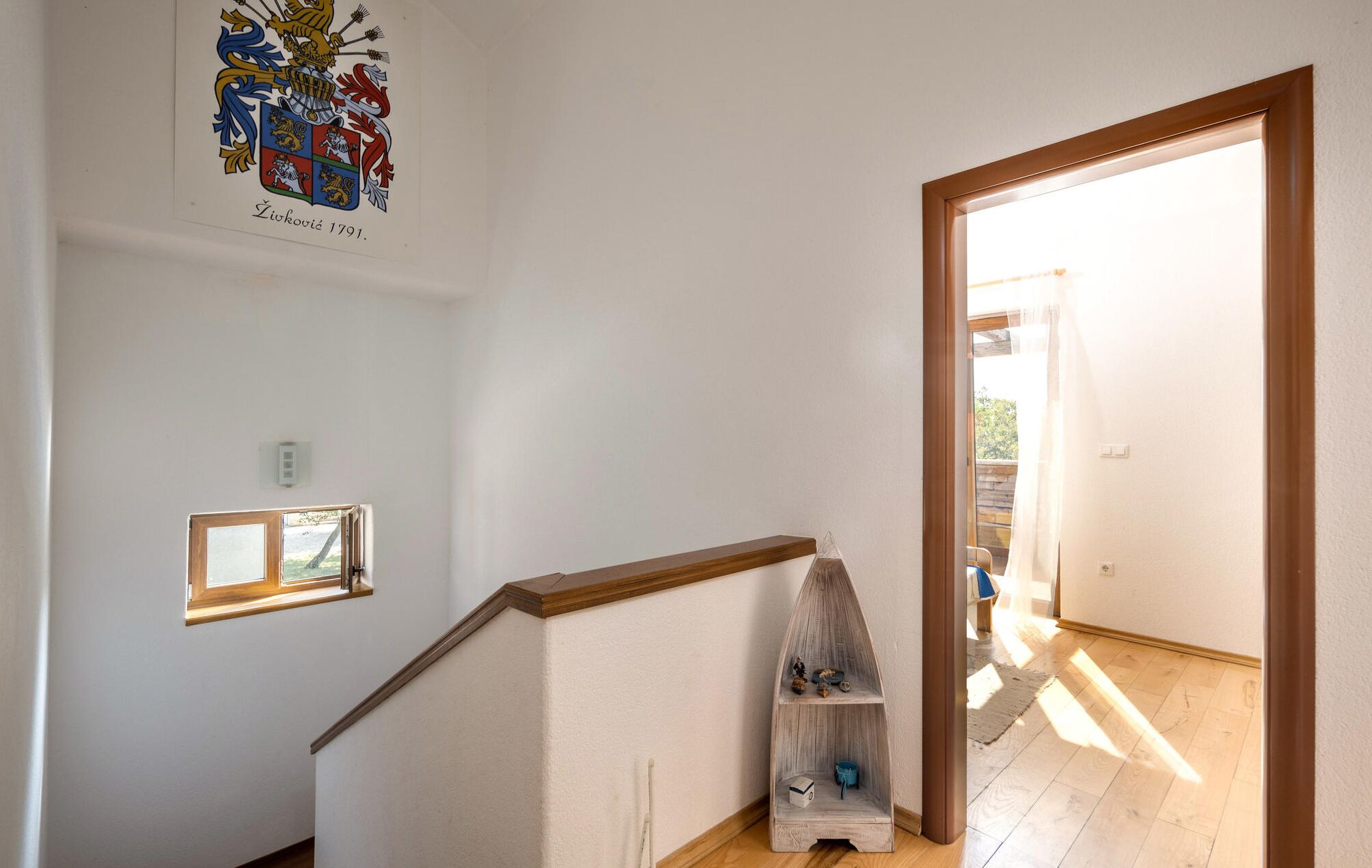 Eine Treppe mit einer Holzhandläufe, einem kleinen Fenster und einem Wappen an der Wand.