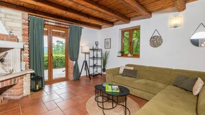 Una sala de estar acogedora con chimenea de ladrillo, un sofá verde, una mesita redonda y un ventanal con vistas a la vegetación.