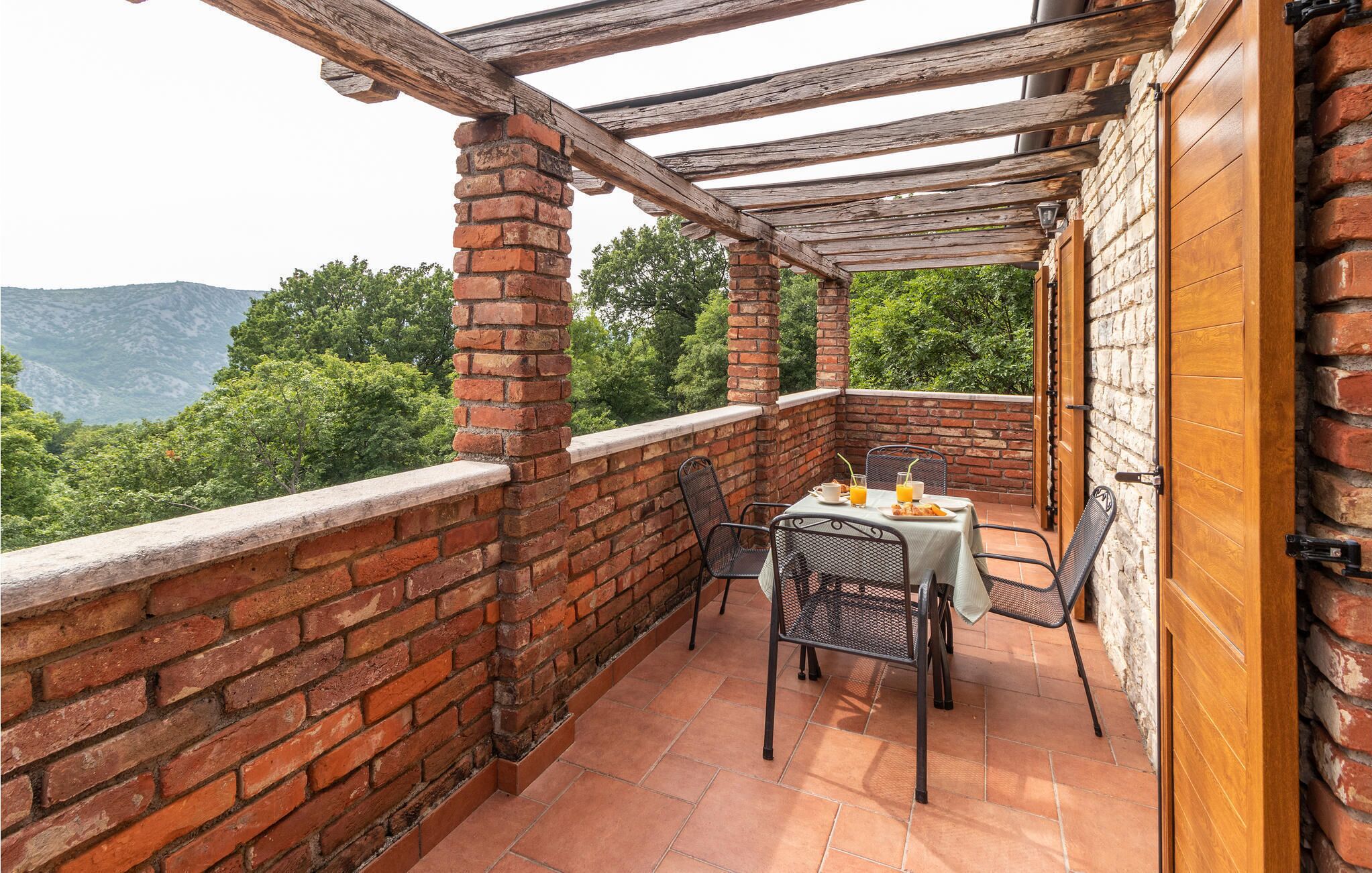 A balcony with a brick wall, wooden beams, and a table with chairs.
