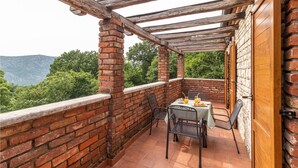 Un balcón con muro de ladrillo, vigas de madera y una mesa con sillas.