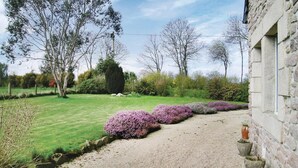 Un jardín con camino de grava, césped verde y arbustos florecientes de color púrpura.