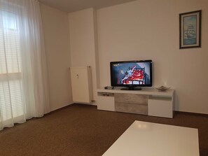 A living room with a flat-screen TV on a white cabinet, a white radiator, a white sofa, and a framed picture on the wall.
