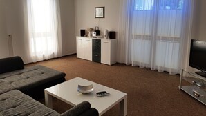 A modern living room with a sofa, a coffee table, a TV, and a kitchen area with cabinets and a refrigerator.