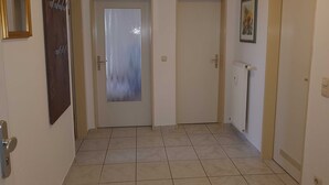 A hallway with two doors, one with frosted glass and another closed. A radiator is on the right wall, and a framed picture hangs above it.