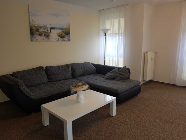 A living room with a dark grey sectional sofa, a white coffee table, and a painting of a beach scene on the wall.