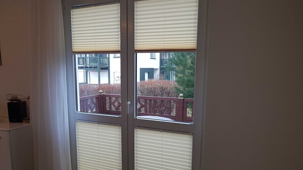 A room with a large window with blinds, a small cabinet, and a view of a balcony with a railing.