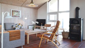 En hyggelig stue med sofa, træbord, fjernsyn, pejs og et stort vindue.