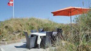Et udendørs siddeområde med fletningsmøbler, et bord, et flag og en parasol.