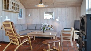 En hyggelig stue med træpaneler, en sofa, stole, et sofabord og et fjernsyn.