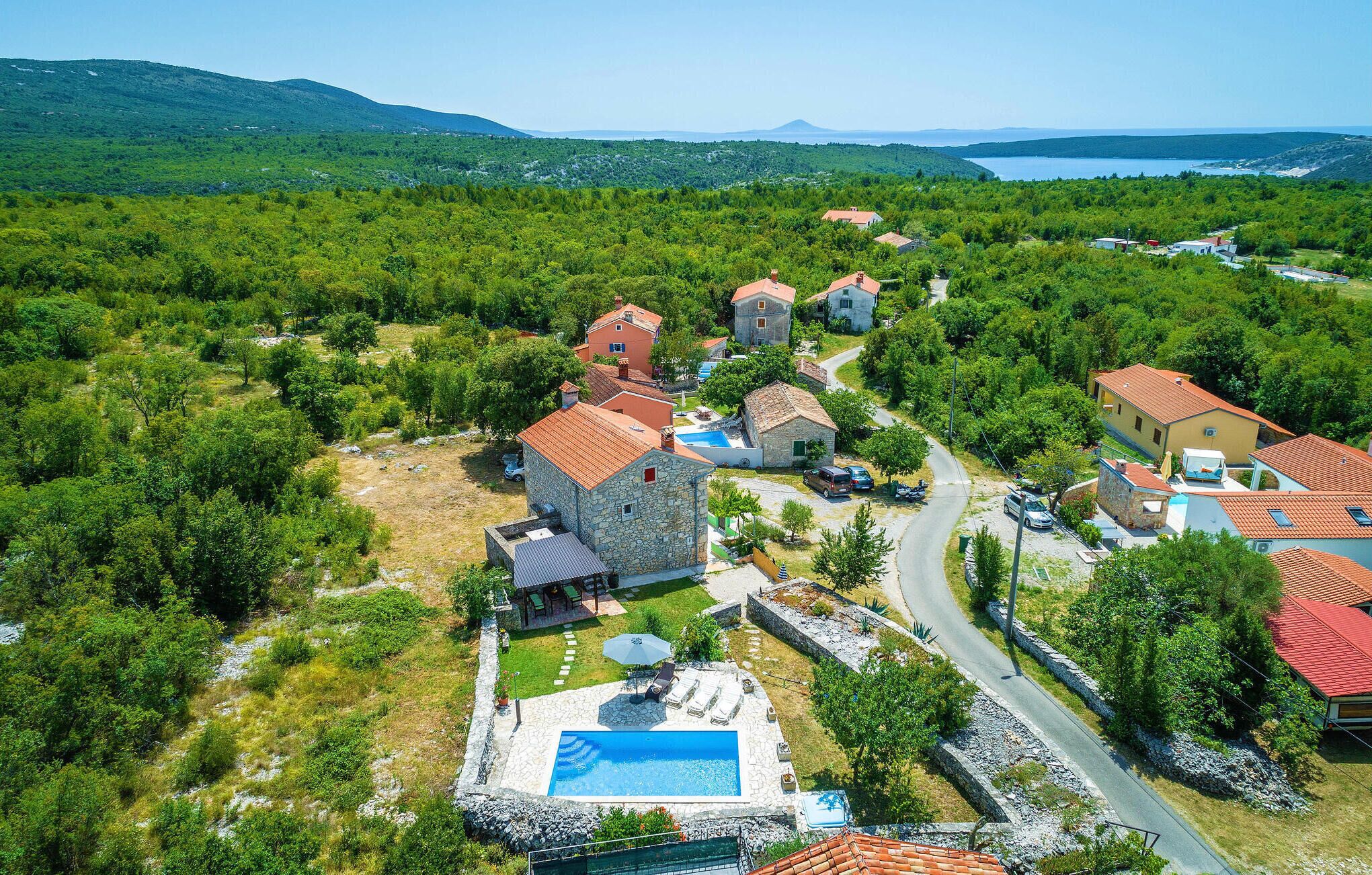 An aerial view of a residential area with stone houses, a swimming pool, and a road.
