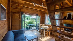 A cozy cabin interior with a wooden floor, a sofa, a small table, and a dining area with chairs.