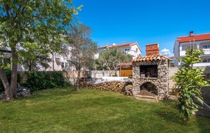 Una cucina esterna in pietra con un camino, immersa in un prato curato e alberi.