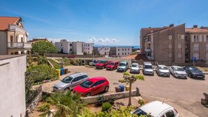 Un estacionamiento con varios autos, un edificio con balcones y una vista despejada del mar al fondo.