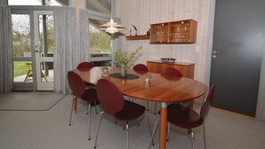 Un coin repas avec une table en bois, des chaises rouges, un vase avec des plantes et une étagère contenant de la verrerie.