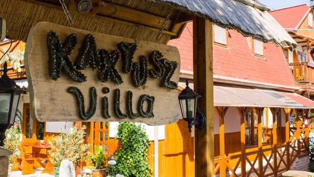 Ein rustikales Holzschild mit dem Schriftzug "Kastel Villa" über einem Holzgebäude mit Wellblechdach.