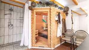 Eine Holzsauna mit Glastür, Duschbereich und Sitzgelegenheit mit Stühlen.