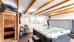Ein Wellnessbereich mit Whirlpool, Holzbalken, einer finnischen Holzs sauna und Blick ins Freie.