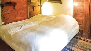 Un lit recouvert d’une courtepointe blanche, dans une pièce aux murs en bois et dotée d’une porte.