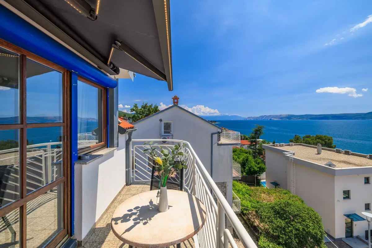 A balcony with a view of the sea, a table with a vase of flowers, and a railing.