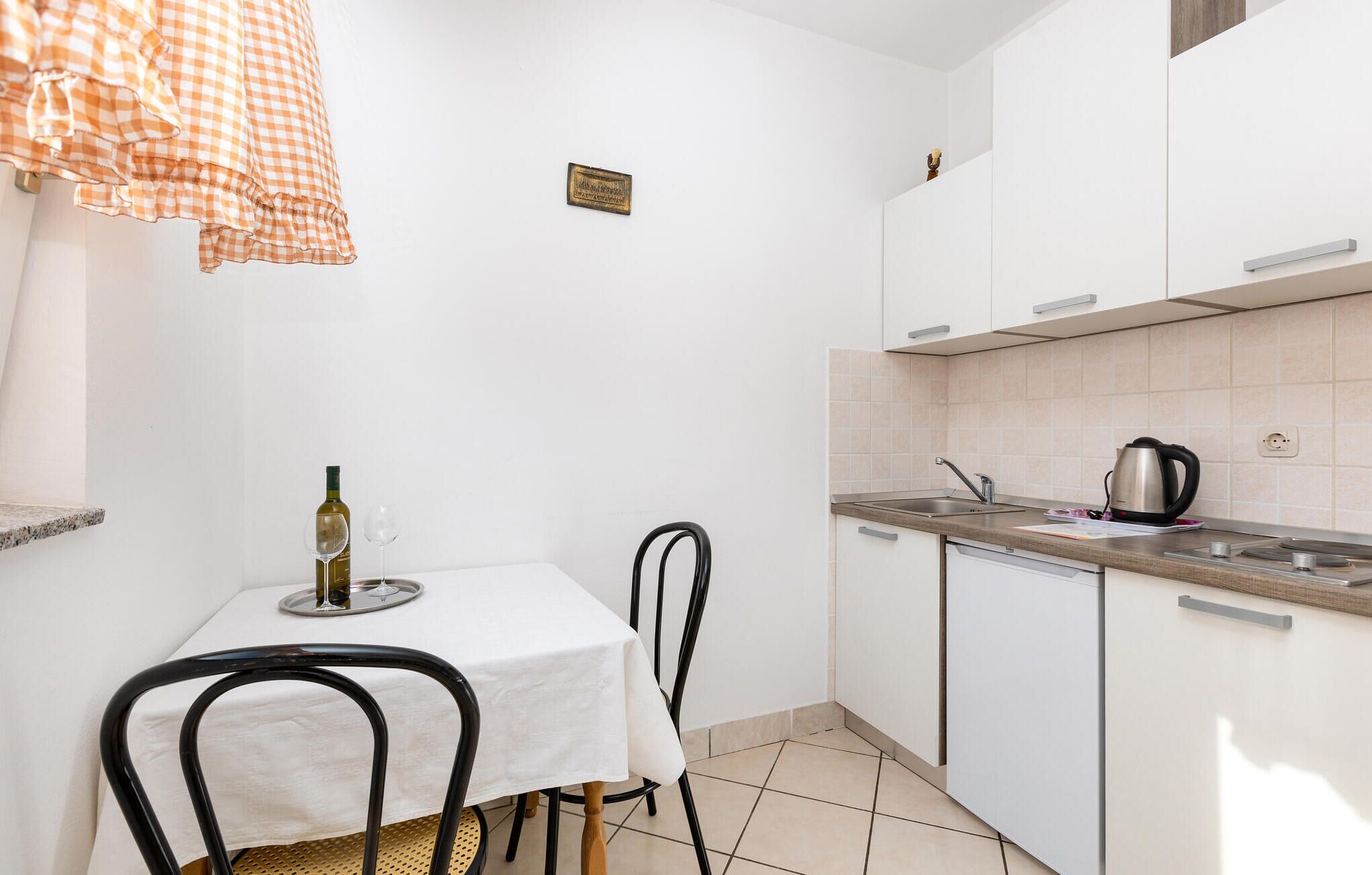 A compact kitchen with white cabinets, a small dining table, and a black chair.