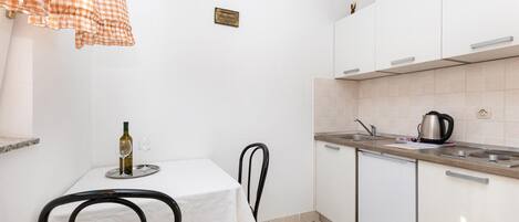 A compact kitchen with white cabinets, a small dining table, and a black chair.