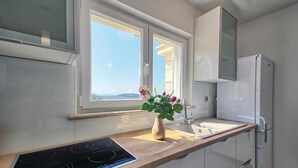 Una cocina moderna con estufa integrada, ventana con vistas al mar y refrigerador blanco.
