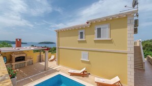 Un edificio de dos pisos con piscina, mobiliario exterior y vista al mar.