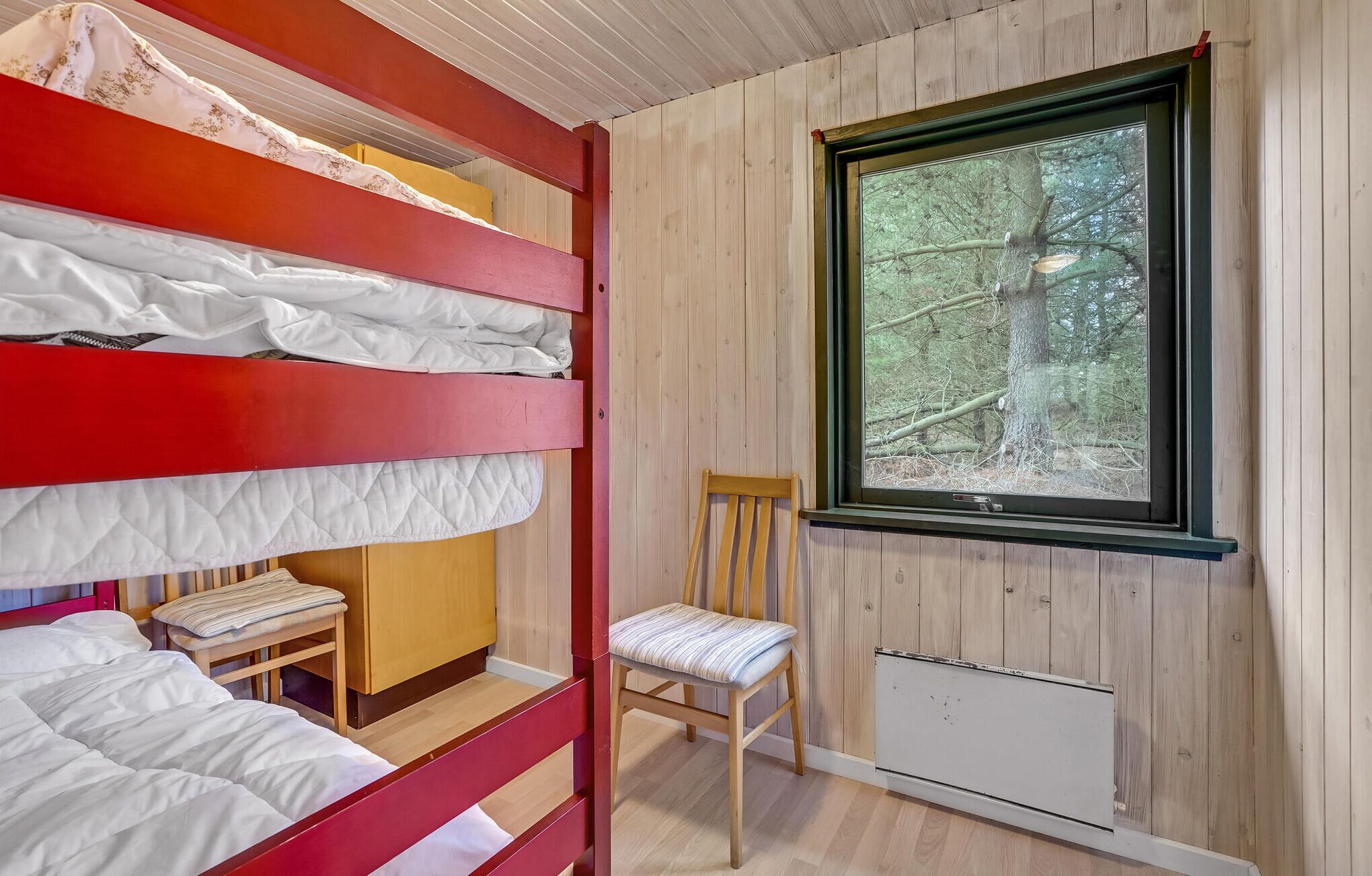 A bunk bed room with a window overlooking a forest.