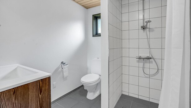A bathroom with a wooden vanity, a toilet, and a shower area with tiled walls and floor.