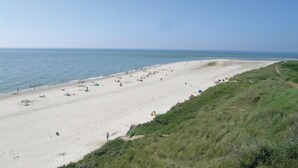 A wide sandy beach with tents and people, grassy dunes, and a clear sky.