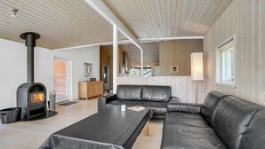A modern living room with a black leather sofa, a black coffee table, and a wood-burning stove. - Nice home in Væggerløse with sauna (Væggerløse)