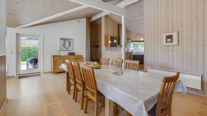 A dining area with a long table, wooden chairs, and a view of the outdoor garden through a glass door. - Nice home in Væggerløse with sauna (Væggerløse)