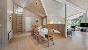 A spacious dining area with wooden flooring and a high ceiling, a kitchen area with a large window, and a seating area with a TV. - Nice home in Væggerløse with sauna (Væggerløse)