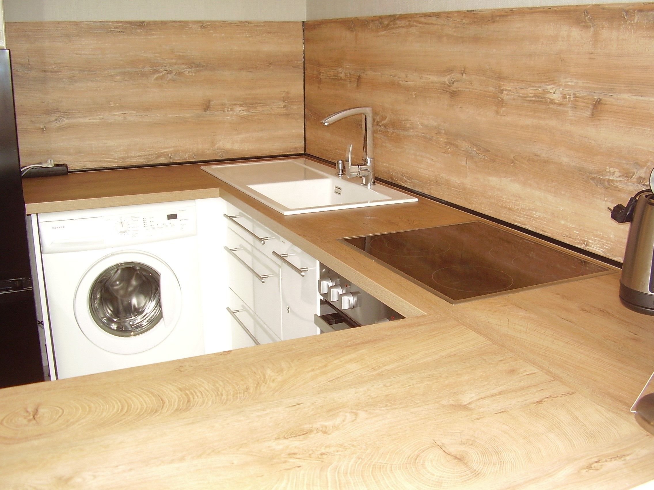 A compact kitchen with a built-in washing machine, a sink, and a stovetop.