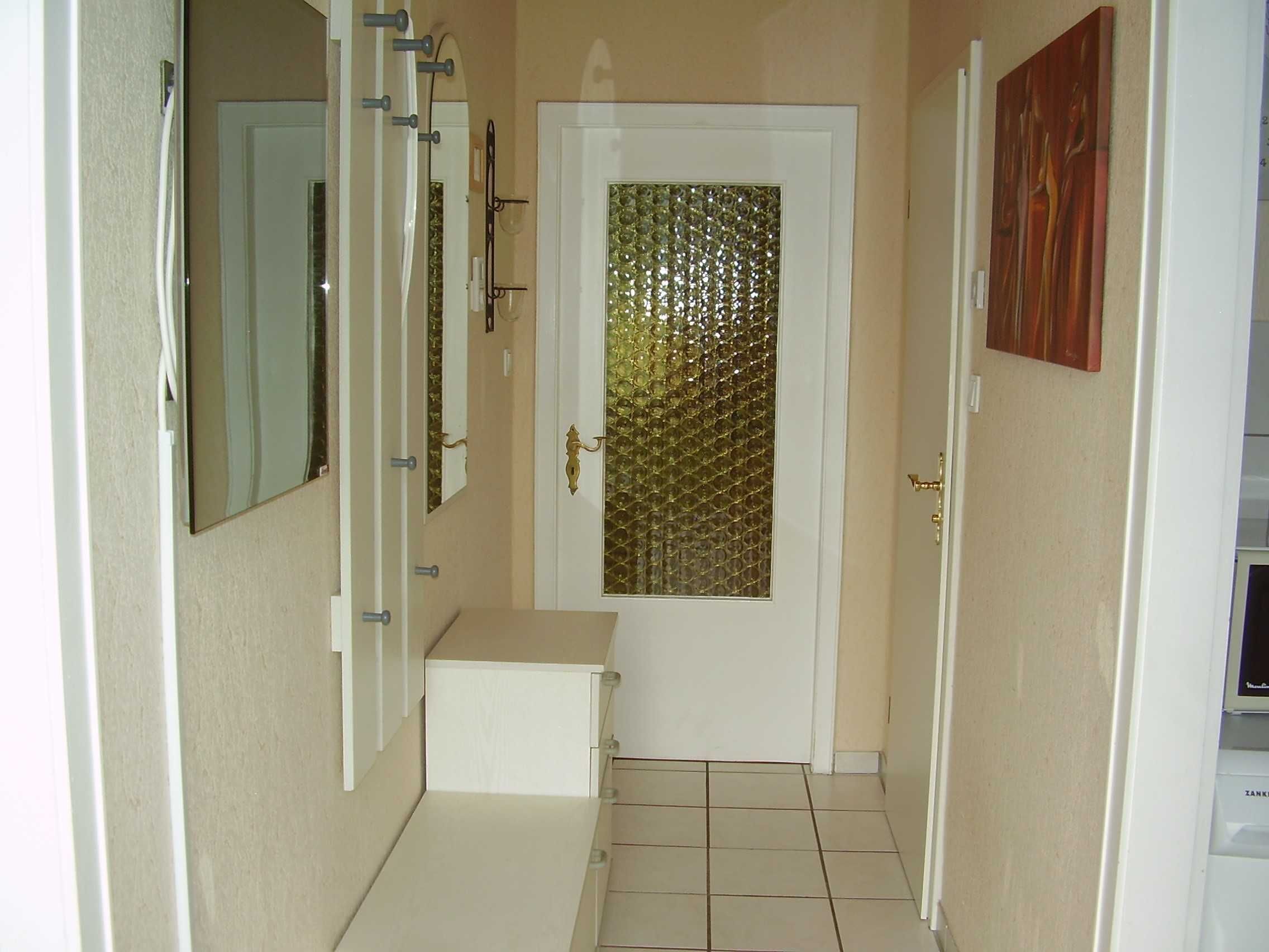 Un couloir étroit avec une porte blanche ornée d’un panneau de verre décoratif.