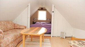 A narrow attic bedroom with a bed, a sofa, a table, and a radiator.