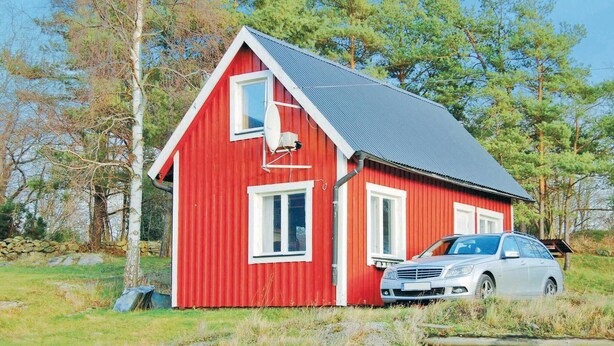 A red house with a grey roof, a car parked in front, and a stone wall in the background.