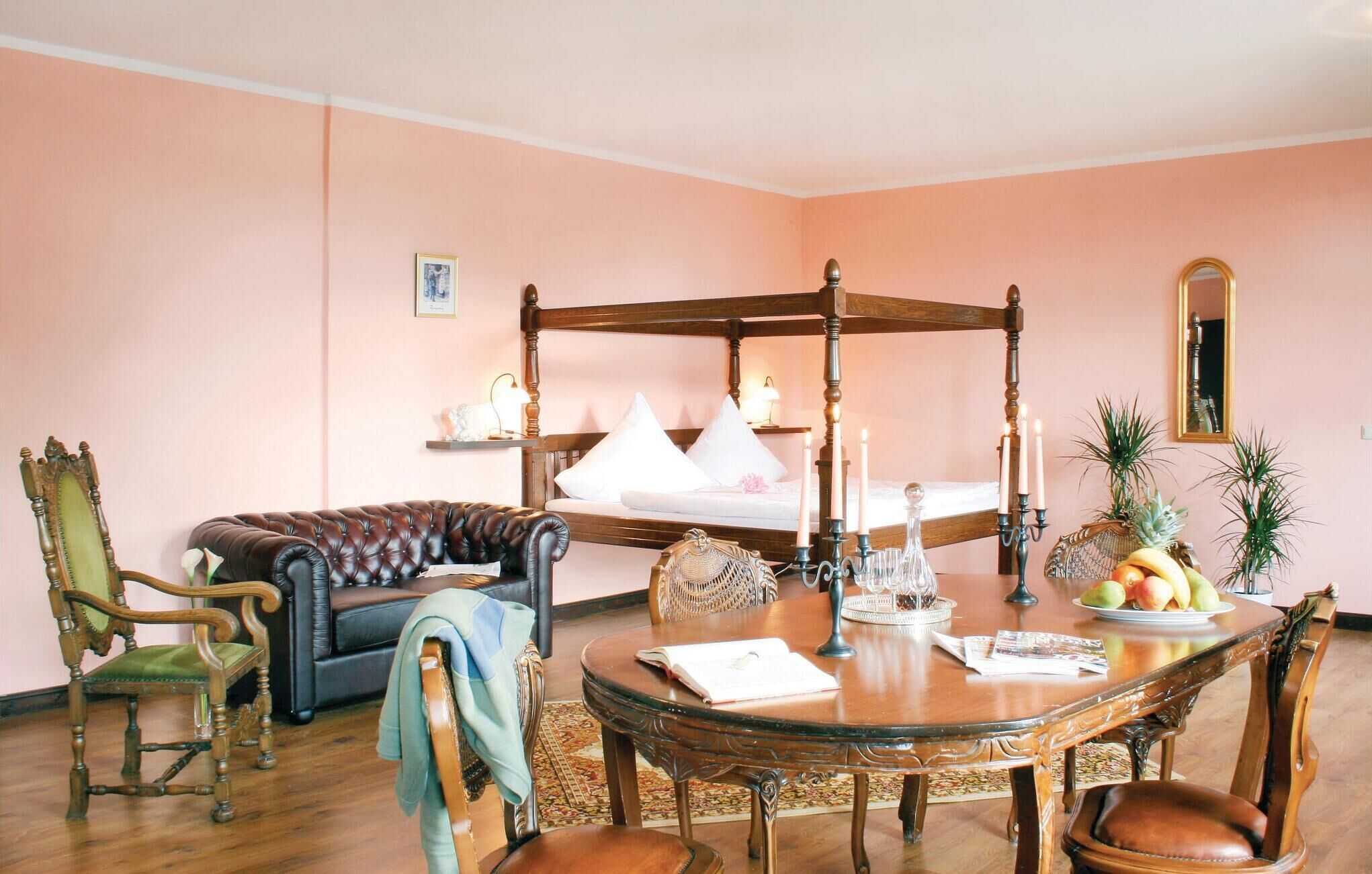 Une chambre avec un lit à baldaquin, une table à manger avec des chaises, un canapé et un fauteuil sur lequel est drapé un manteau.