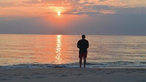 Henkilö kalastaa auringonlaskun aikaan rannalla.