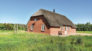 Punatiilinen talo, jossa on olkikatto, satelliittiantenni ja savupiippu.